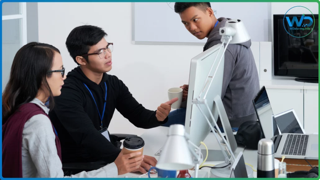 Dans un espace de travail contemporain, trois collaborateurs dialoguent devant un écran, renforçant la dynamique collective au cœur de l’environnement professionnel | wdata-mg.info